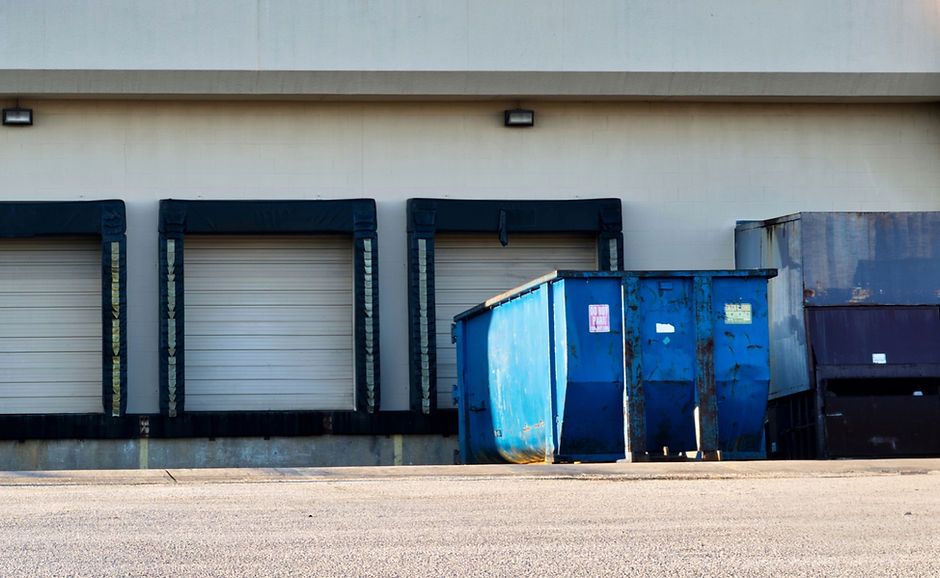 Closed dock doors at the back of a generic industrial warehouse building with blue dumpste