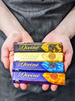 Person holding four Divine chocolate bars in dark, white, milk and orange flavours.