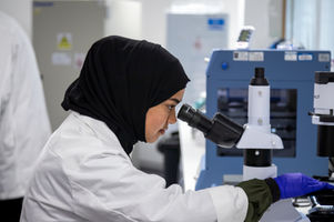 Researcher in a lab coat using a microscope in a laboratory workspace.