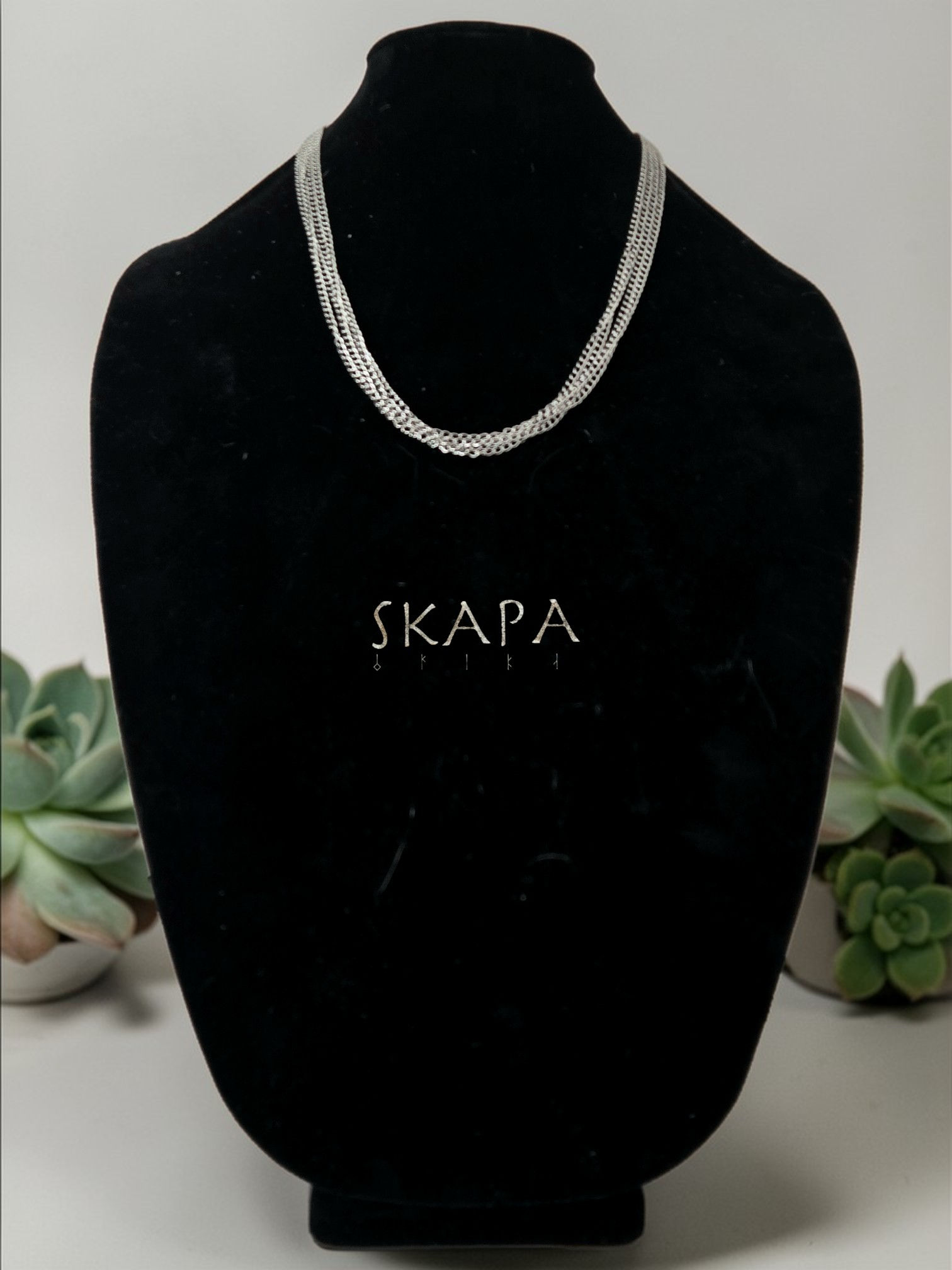 A silver-toned, 3mm multi-strand necklace displayed on a black jewelry bust. The brand name SKAPA is visible below the neckla