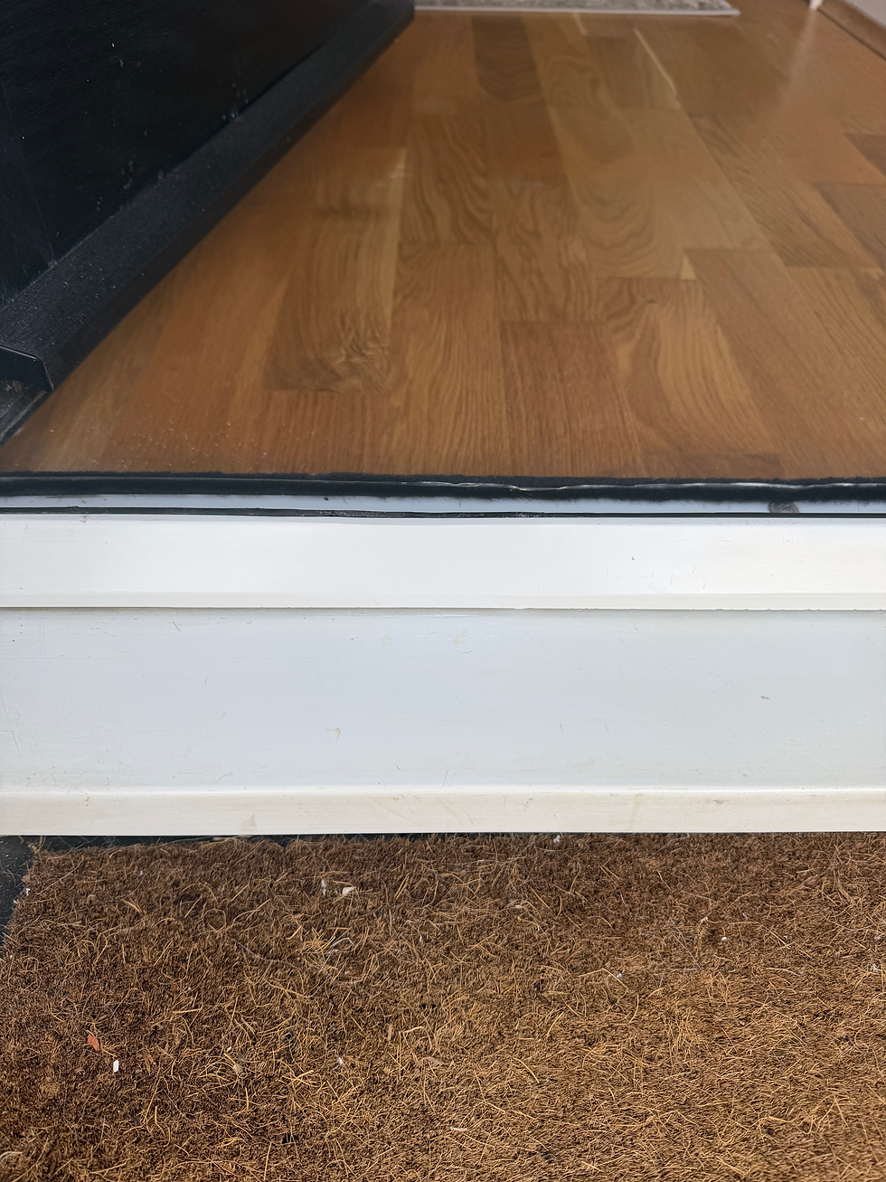 White doorway threshold separating interior wood laminate flooring from an exterior coir doormat