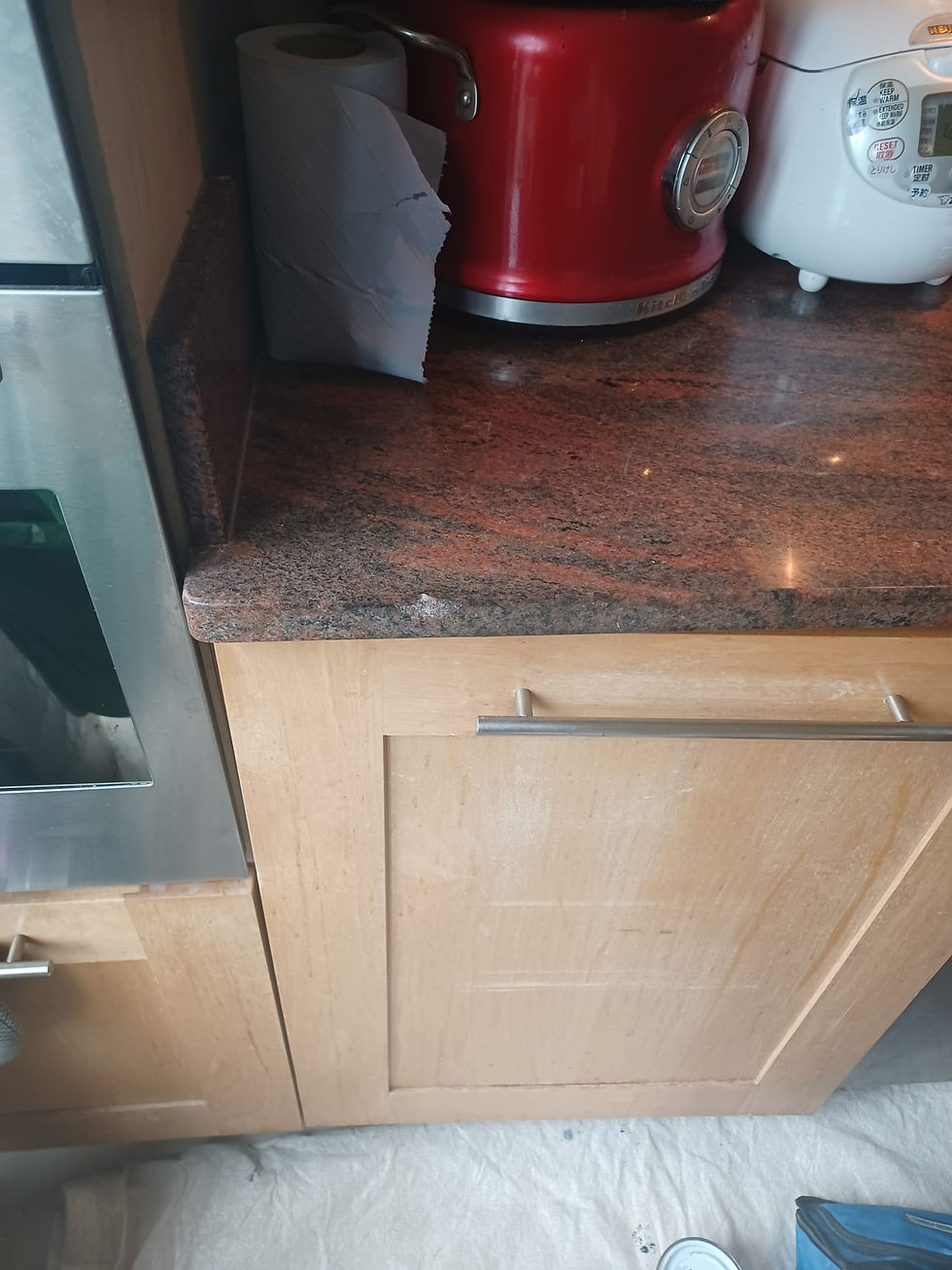 Red granite countertop over wooden kitchen cabinets with small chip damage along the front edge