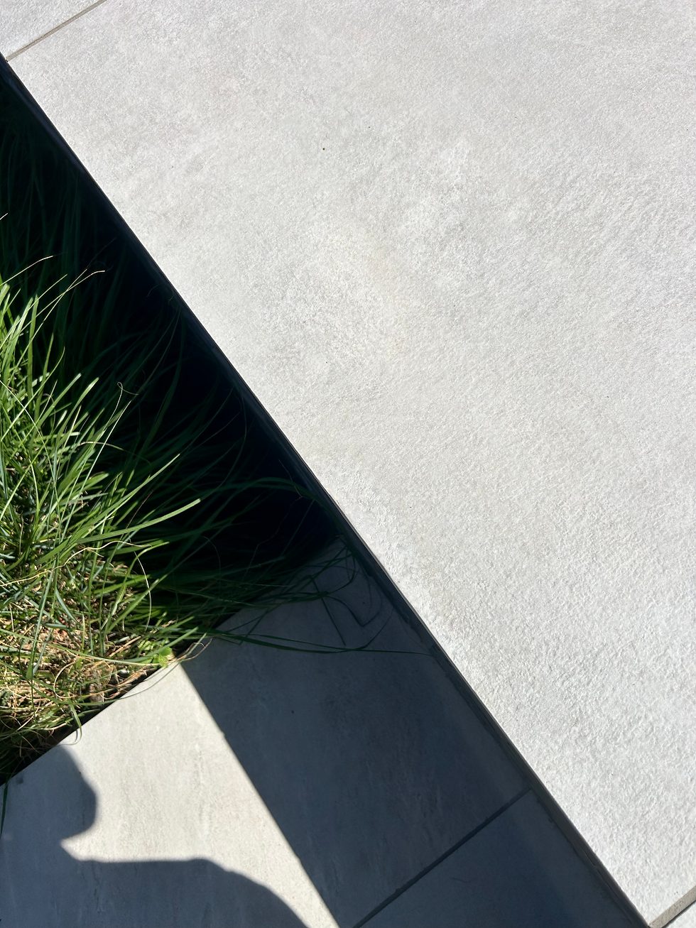 Light grey textured stone patio paving slab edging above a small garden patch with ornamental grass