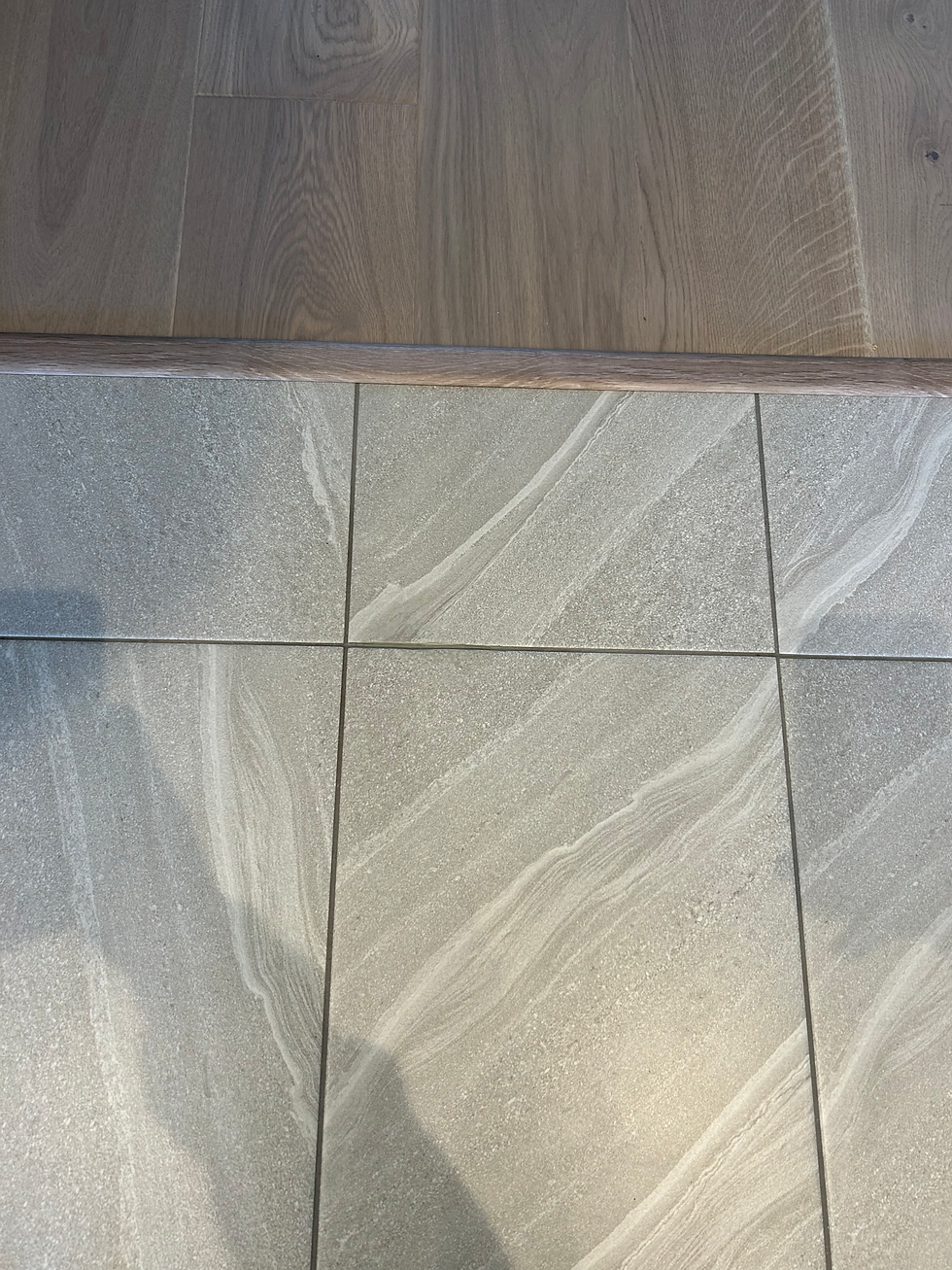 Grey stone pattern floor tiles transitioning to wood laminate flooring across a threshold strip