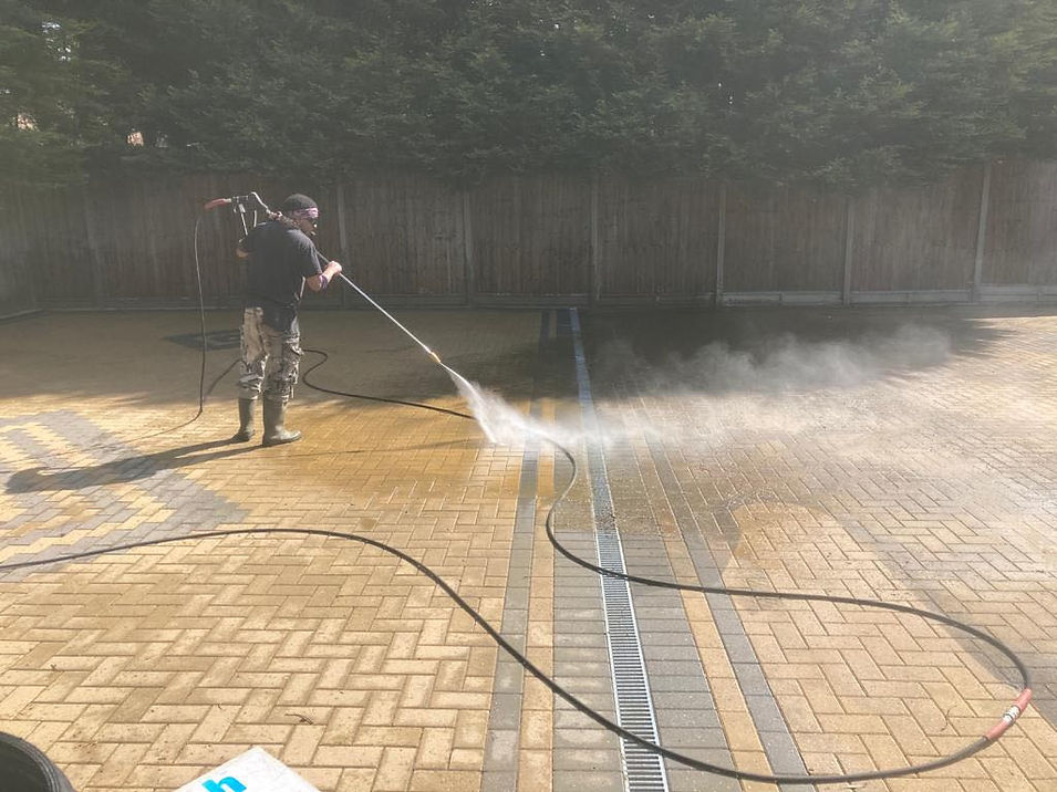 A worker using a high-pressure power washer to clean a paved driveway