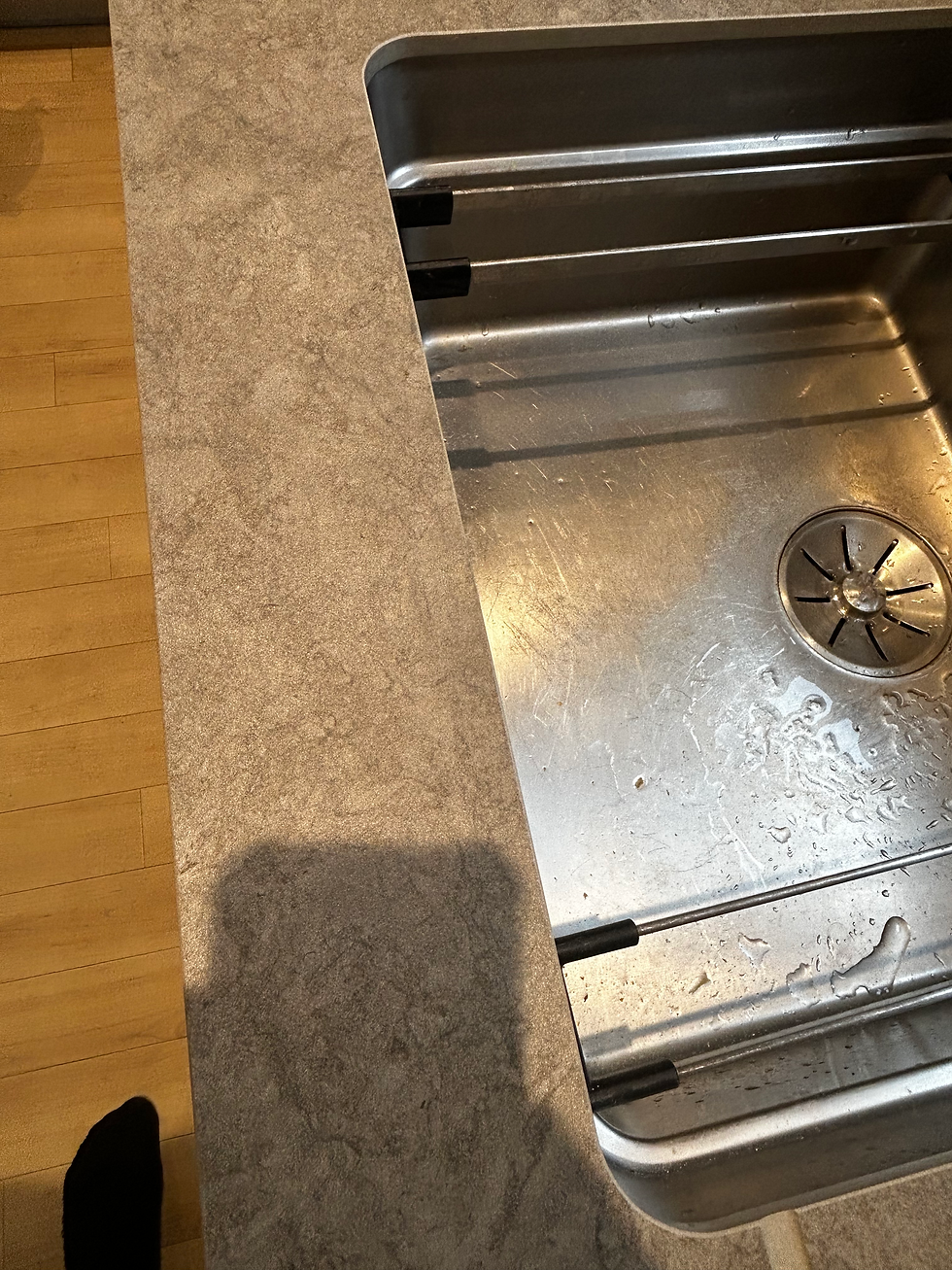 Stainless steel undermount kitchen sink set into a textured grey composite countertop above light wooden flooring