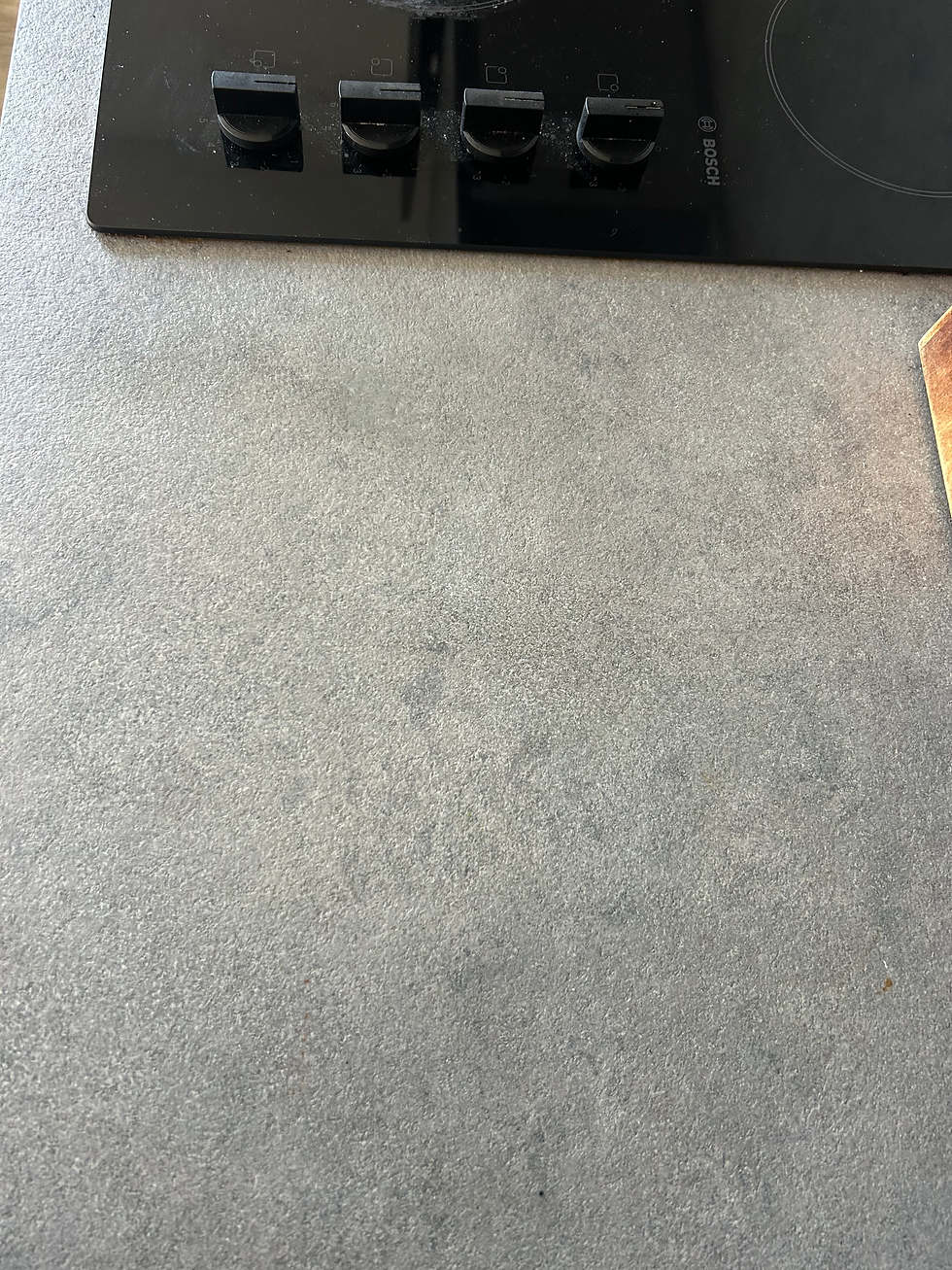 Black glass electric stovetop with control knobs set into a grey stone-effect laminate countertop