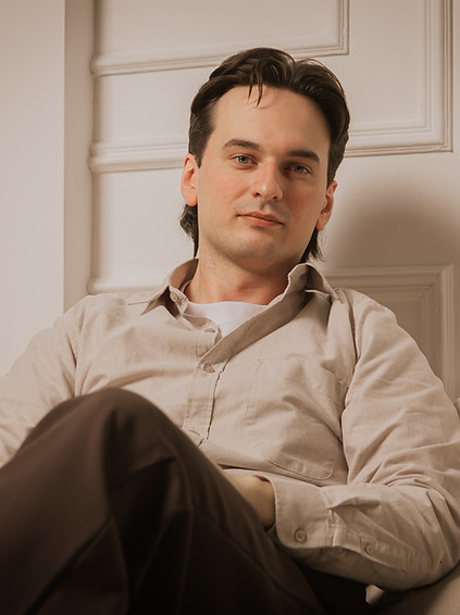a young psychotherapist with a half-smile on his face sits on the couch in the relaxed pose