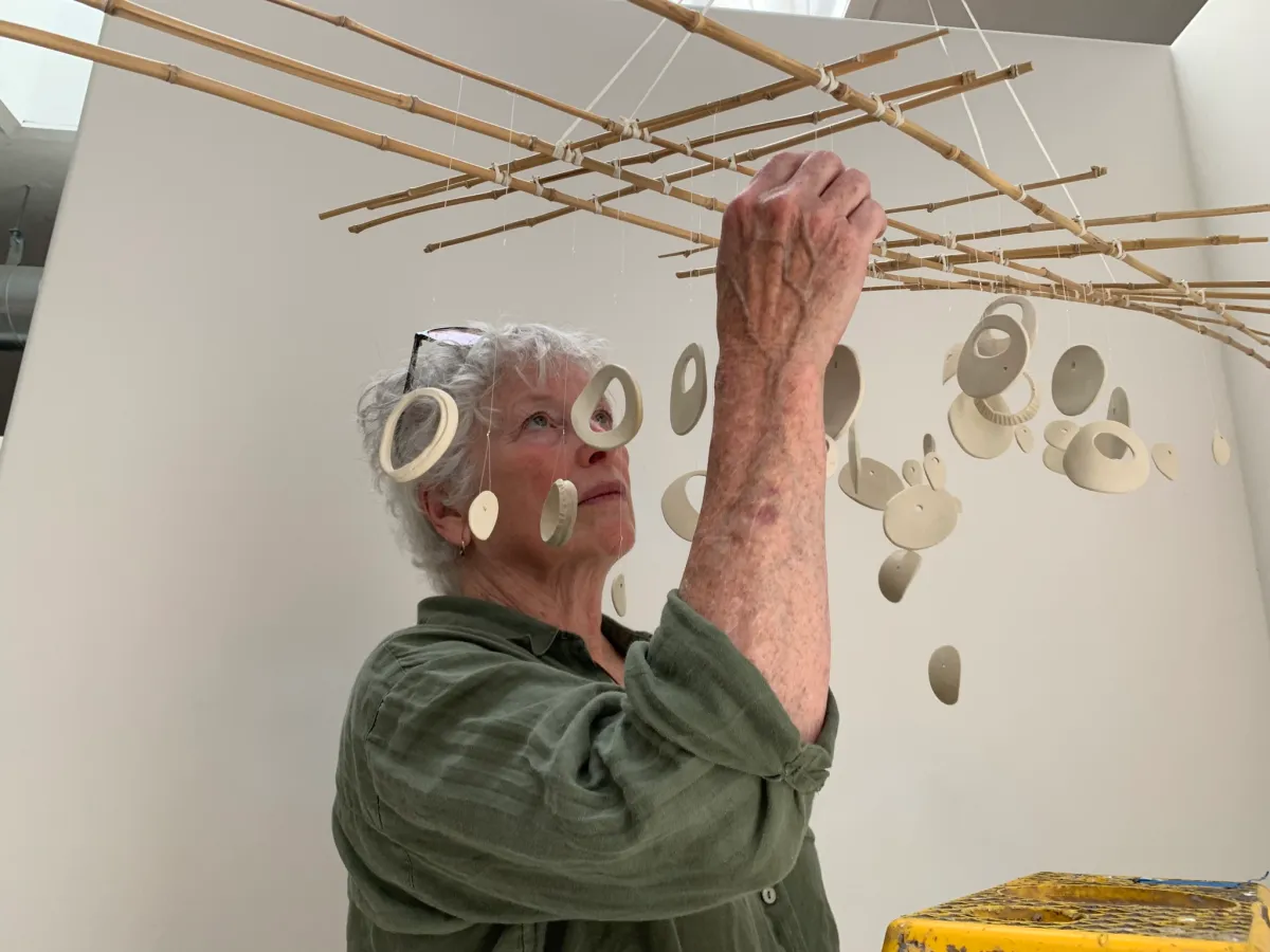 the artist adjusts elements of her mobile as she hangs it for the gallery show