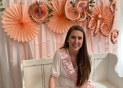 A wedding shower is in progress - the bride wearing a banner that says "bride" across her shoulder, seated in front of a wall decoration that says "bride"