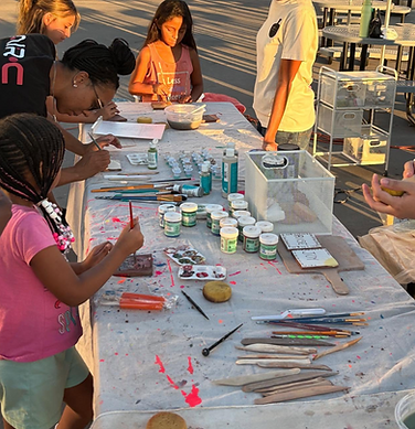 Materials for painting pottery are on a table, people are working on the art