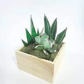 A wooden box, filled with dirt, holds a collection of stained glass ornaments that look like 3 dimensional succulents. 
