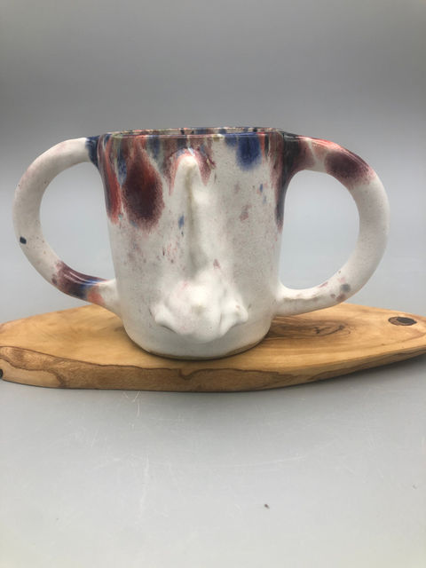 Coffee mug with two large handles, white with prominent sculpted nose and  glaze dripping from the rim.