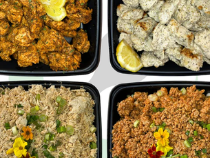 Four black trays with colorful dishes: top left spicy chicken with lemon, top right grilled chicken with dip, bottom rice dishes with flowers.