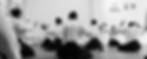 Foto panorâmica em preto e branco mostrando uma linha de alunos deitados/sentados em seiza de costas, observando o instrutor à frente no tatame amplo. A imagem destaca a excelente presença feminina e a estrutura do en dojo para turmas de aikido para mulheres e público geral em Pinheiros.