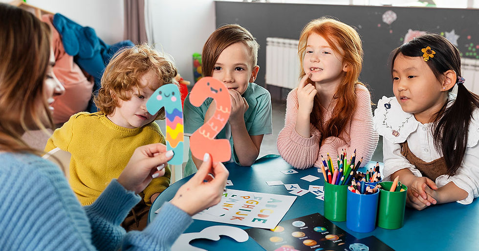 Four children watch a teacher holding colorful cutouts of numbers 1 and 2 at a table with pencils, creating a playful learning scene at Kids Wonderland Summer Camp