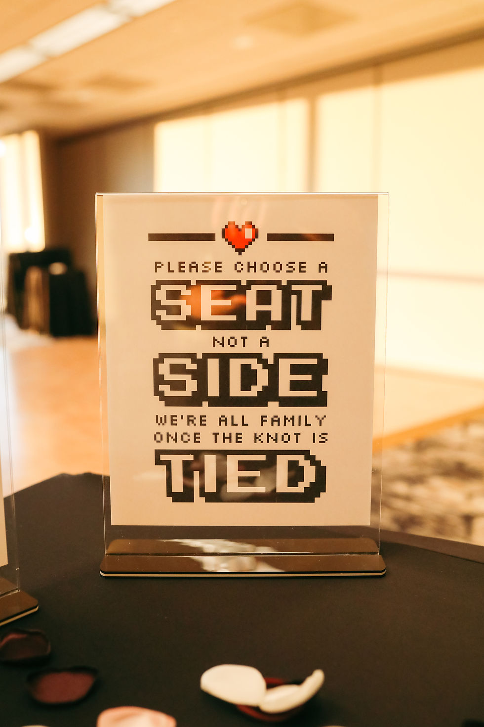 A sign stating "Please choose a seat, not a side. We're all family once the knot is tied.
