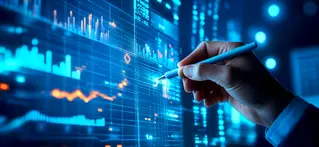 A hand holding a pen interacts with a futuristic digital screen displaying various data visualizations and analytics charts. The glowing blue interface includes bar graphs, line graphs, and geometric data points, representing financial or business intelligence metrics in a high-tech environment. The scene conveys the concept of data analysis, strategic planning, and digital transformation.