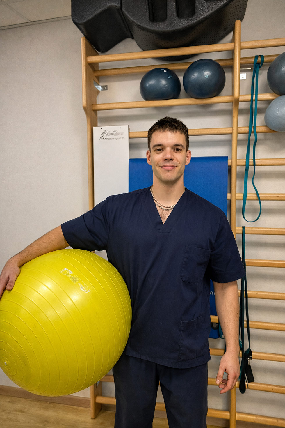 Fisioterapista sorridente con palla gialla in ambiente di riabilitazione.