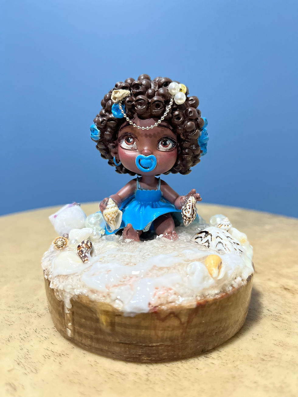 Boneca afro com vestido azul e detalhes, em cima de bolo.