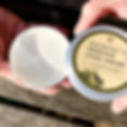 Hand removing the lid of a large tin of hand cream to show the rich white cream inside
