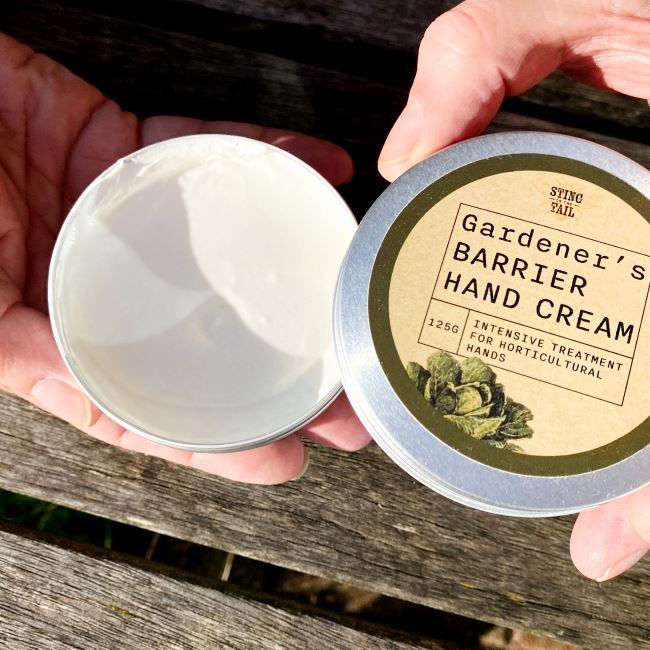 Hand removing the lid of a large tin of hand cream to show the rich white cream inside