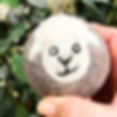 Hand holding a 100% wool dryer ball with a cute sheep face against a background of leaves