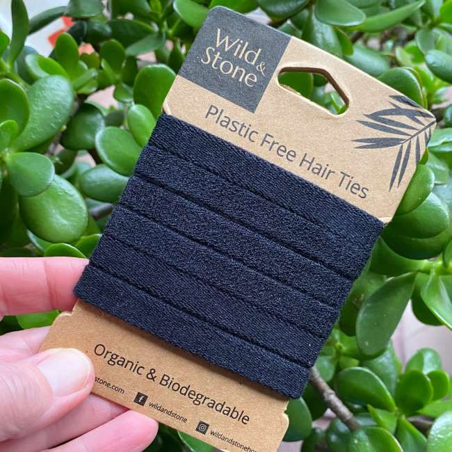 Thumbnail: Hand holding a pack of six black plastic-free hair bands in front of green leaves
