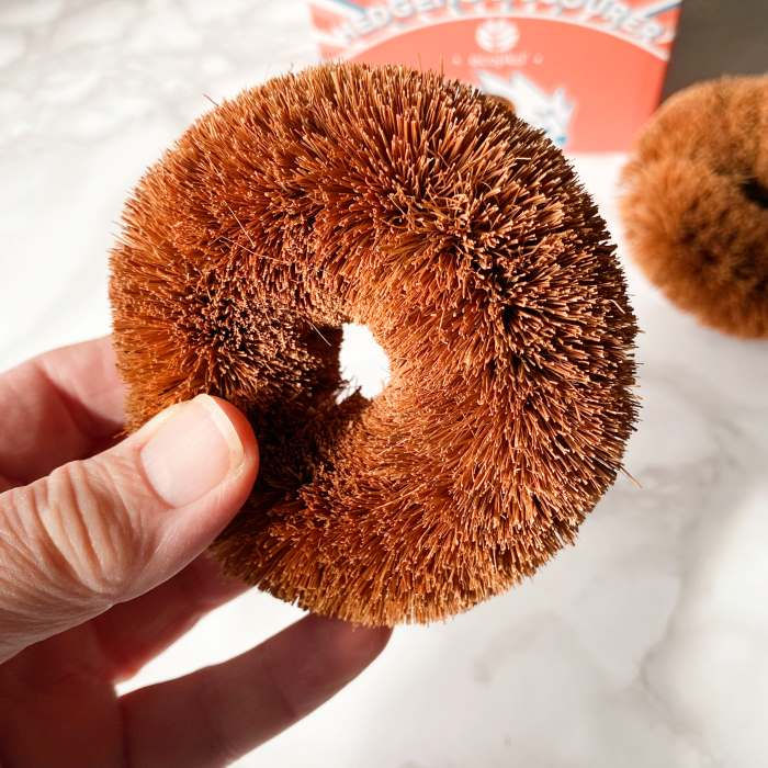 Hand holding a single coconut scourer above a kitchen counter