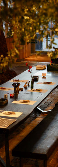Long, dark wooden table with linocut printmaking tools and plants