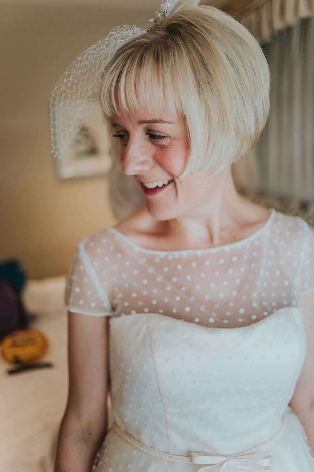 Bride smiling having her dress fastened at Holdsworth House