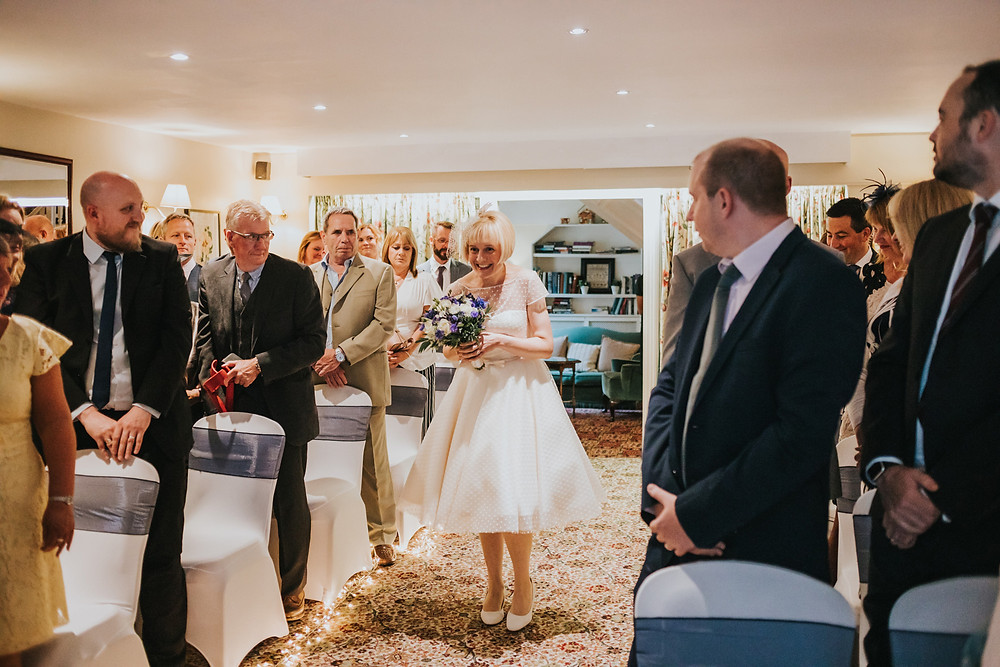 Bride smiling walking down the aisle by herself at holdsworth house
