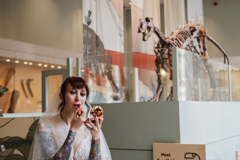 Bride applying lipstick next to a dinosaur at manchester Museum wedding