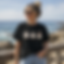 Woman wearing a black seagull graphic T-shirt on a coastal boardwalk overlooking the sea,