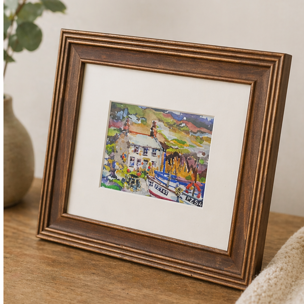 Framed Treen Cove coastal cottage print by Ellen Visser styled on wooden surface with books and ceramic decor