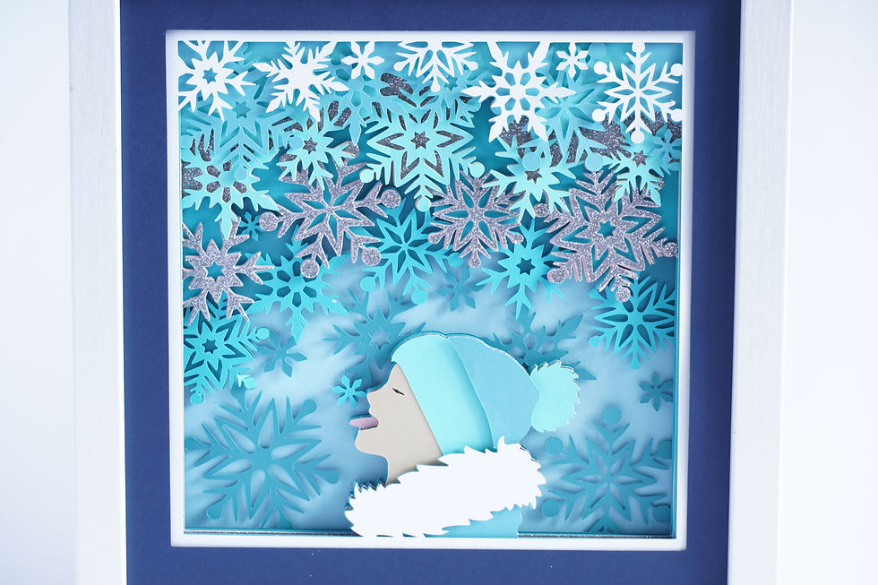 Thumbnail: White framed 3d shadow box of child catching snowflakes on tongue in shades of blue and silver