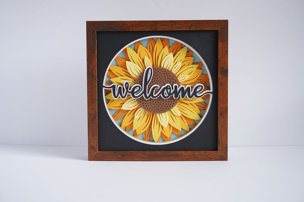 Thumbnail: Brown framed 3D shadow box of a yellow and orange layered sunflower with the word, "welcome" in black