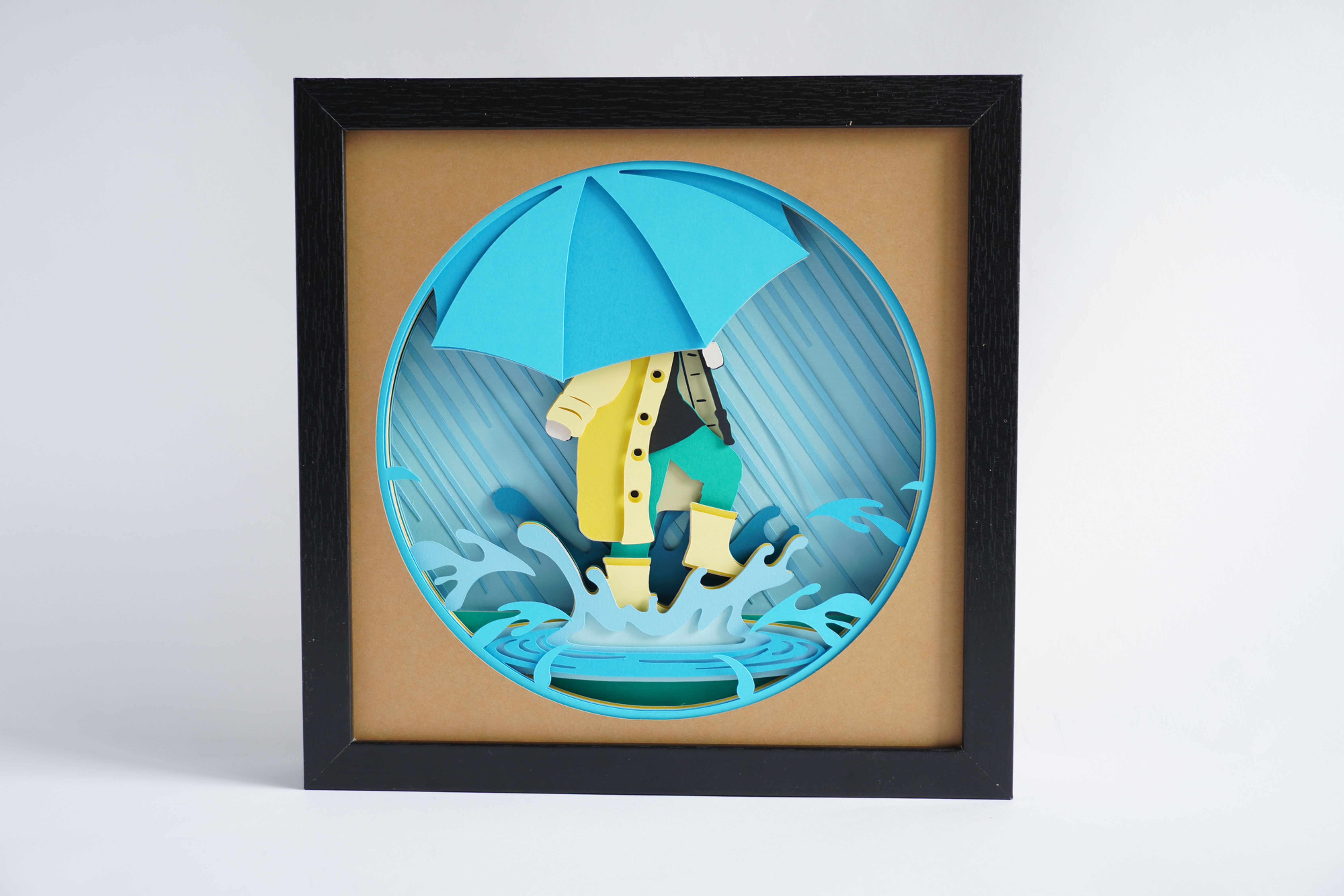 Black framed 3D shadow box of a person splashing in a puddle while holding an umbrella