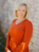 Photo of Margaret, the Practice Manager at LKN Wellness in Mooresville, NC. She is smiling, wearing an orange dress, and standing in front of a whitewashed brick wall.