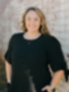 Photo of Caitlyn, the LKN Wellness Phlebotomist, smiling in a black shirt and standing in front of a whitewashed brick wall in Mooresville, NC