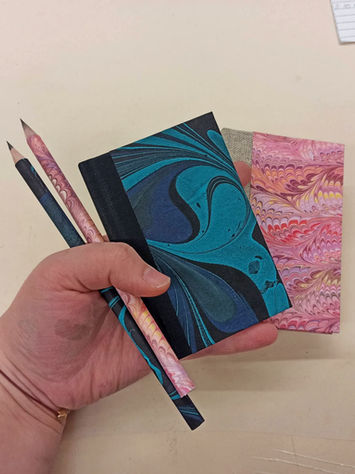 Miniature handbound address books in marbled blue and pink papers, shown together with matching handmade pencils .