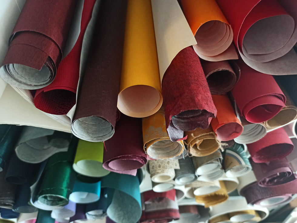 Nahaufnahme gerollter Buchbindematerialien, darunter dekorative Papiere, Buchleinen und farbige Blätter in kräftigen, lebendigen Tönen.