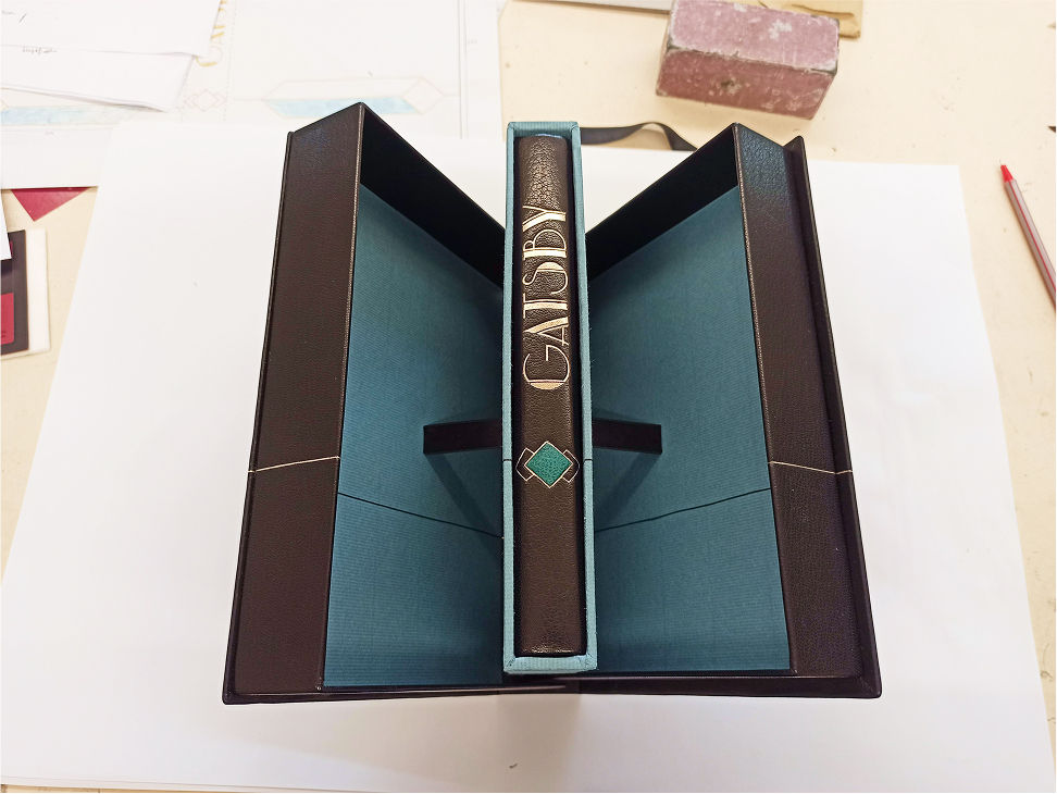 Eine handgefertigte Kassette in Türkis und Dunkelbraun enthält eine edel gebundene Ausgabe von „Gatsby“ mit Goldprägung und dekorativem Einlageelement am Buchrücken.