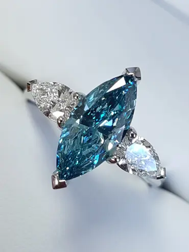 A marquise shaped blue diamond central stone, with a white, pear-shaped diamond either side of it, in a traditionally styled platinum three-stone ring.