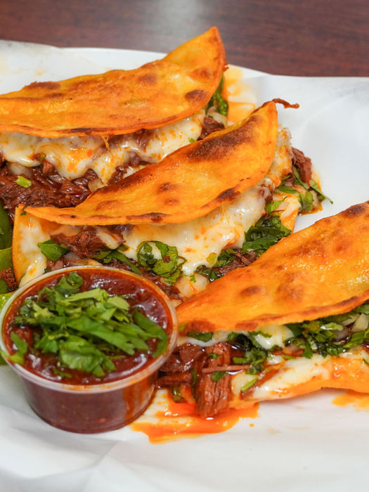 Three birria tacos with cheese, cilantro, limes, and sauce