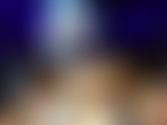 A group of young frum children excitedly reach up together to hold and wave a large Israeli flag during a festive indoor celebration. The children, some wearing kippot and colorful clothing, stand close together with joyful expressions under dramatic blue lighting, surrounded by other kids and more Israeli flags in the background, capturing a moment of proud unity and simcha.