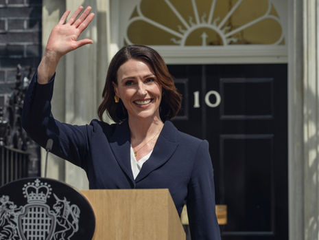 Suranne Jones waving her hand and greeting people behind a podium.