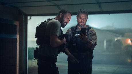 Ben Affleck and Matt Damon wearing police gear and looking at a phone in a garage.