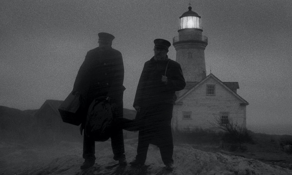 Robert Pattinson and Willem Dafoe out in a storm with the lighthouse behind them