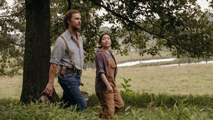 Matthew McConaughey and Angelina LookingGlass walking outside in front of a tree as he carries buckets.